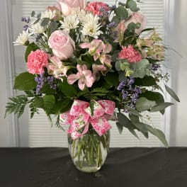 Pink roses and mixed flowers in a glass vase with a pink ribbon