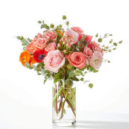 Pink and peach roses with red and orange blooms in a clear glass vase