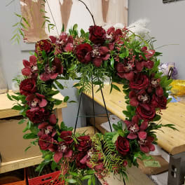 Heart-shaped floral wreath with deep red roses and orchids on a stand