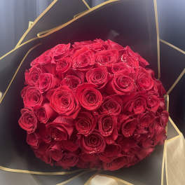 Round bouquet of red roses wrapped in black and gold paper