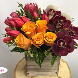 Bouquet of orange roses, red tulips, and burgundy orchids in a wooden box