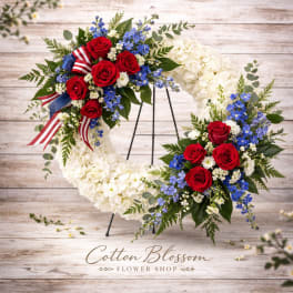 White floral wreath with red roses and blue flowers on a stand