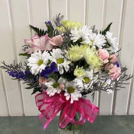 Mixed bouquet of daisies, roses, and alstroemeria in a glass vase with a pink ribbon