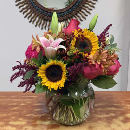 Mixed bouquet with sunflowers, lilies, and pink roses in a glass vase