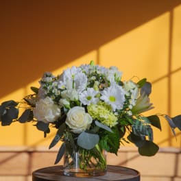White flowers in a clear glass vase with dark foliage
