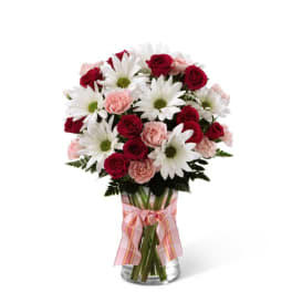 Bouquet of red roses, pink carnations, and white daisies in a glass vase