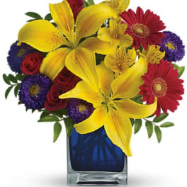 Bouquet of yellow lilies, red roses, and purple daisies in a blue glass vase
