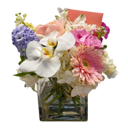 Mixed pastel bouquet in a clear glass vase with orchids, roses, and gerbera daisies