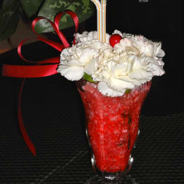 White carnations in a red drink glass with striped straws and ribbon