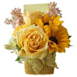 Yellow roses and sunflowers in a woven basket with pink accent flowers