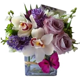 Bouquet of purple roses and white orchids in a square glass vase
