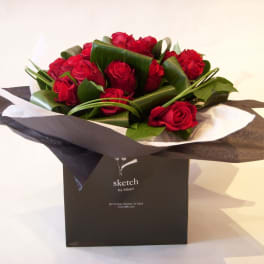 Red roses arranged in black and white wrapping inside a black gift bag