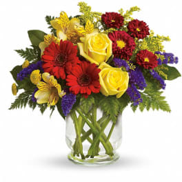 Bouquet of yellow roses, red daisies, and purple filler in a glass vase
