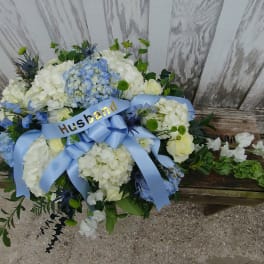 White and blue floral arrangement with a blue ribbon labeled Husband