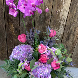 Pink orchids and roses arranged with lavender hydrangeas in a basket