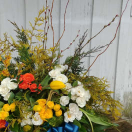 Large mixed floral arrangement with white, yellow, and orange blooms and a blue ribbon
