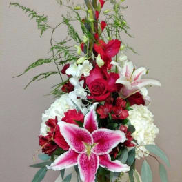 Tall red, white, and pink flower arrangement with lilies, roses, orchids, and hydrangeas in a clear glass vase.