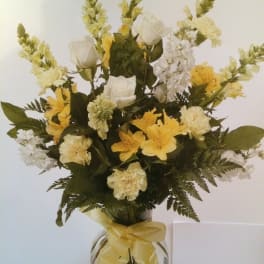 Yellow and white floral arrangement in a clear glass vase with a ribbon