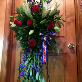 Tall floral standing spray with red roses, white lilies, and blue flowers