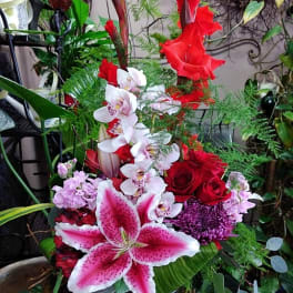 Tall mixed floral arrangement with red roses, pink lilies, and white orchids in a glass vase