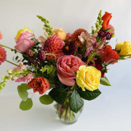 Mixed bouquet of roses, dahlias, and zinnias in a clear glass vase