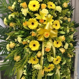 Large yellow floral standing spray with gerberas, roses, lilies, and ribbon