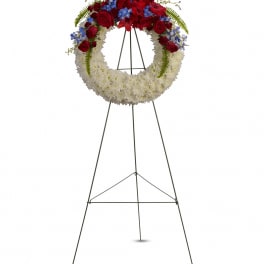 Standing floral wreath with red roses, white flowers, and blue accents on a metal easel