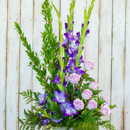 Tall floral arrangement with purple flowers and pale pink roses in a square vase