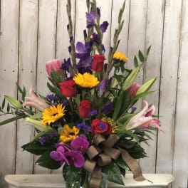Tall mixed bouquet in a glass vase with roses, lilies, orchids, and yellow daisies