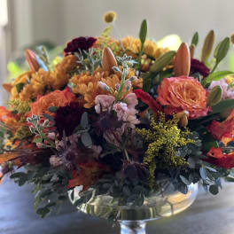Autumn bouquet in a clear glass pedestal vase with orange and burgundy blooms