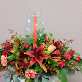Mixed floral arrangement in a clear glass vase with an orange candle