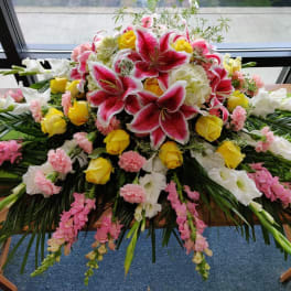 Large floral casket spray with pink lilies, yellow roses, and white blooms