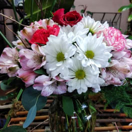 Mixed bouquet of white daisies, pink alstroemeria, and red roses in a glass vase