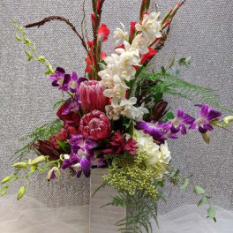 Tall floral arrangement with purple orchids, white orchids, and red tropical blooms in a white vase
