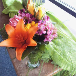 Bouquet of orange lilies, pink flowers, and yellow blooms in a glass vase