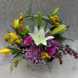 Basket arrangement with white lily, purple mums, pink carnations, and yellow tulips.