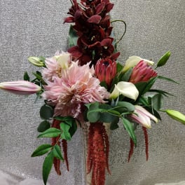 Tall floral arrangement with pink dahlias, burgundy orchids, and lilies in a glass vase