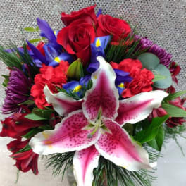 Bouquet of red roses, pink lilies, and purple flowers in a glass vase