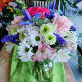 Mixed bouquet of pink, white, purple, and blue flowers in a glass vase
