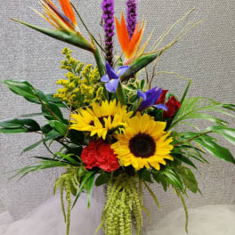 Tropical bouquet with sunflowers, bird of paradise, and purple spikes in a glass vase