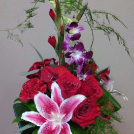 Tall bouquet of red roses, pink lily, and purple orchids in a glass vase