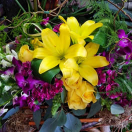 Bright yellow lilies and purple orchids arranged with roses in a decorative basket.