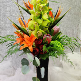 Tall tropical bouquet with green orchids, orange lilies, and red roses in a black vase