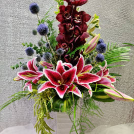 Tall floral arrangement with pink lilies, burgundy orchids, and blue thistle in a vase