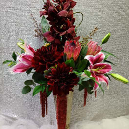 Tall floral arrangement with burgundy orchids and pink lilies in a gold vase