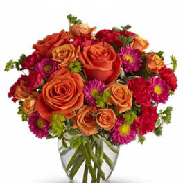 Orange roses and pink daisies arranged in a clear glass vase