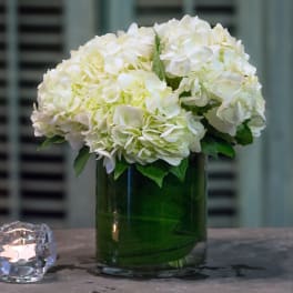 White hydrangea bouquet in a green glass vase beside a candle