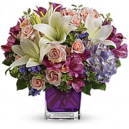 Bouquet of lilies, roses, and hydrangea in a purple glass vase