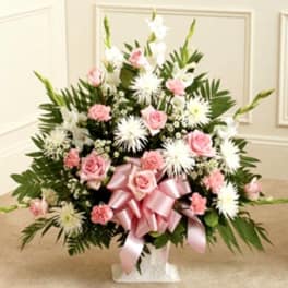 Pink roses and white flowers arranged in a vase with a pink ribbon