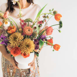 Mixed bouquet in a white vase with orange, pink, purple, and yellow flowers